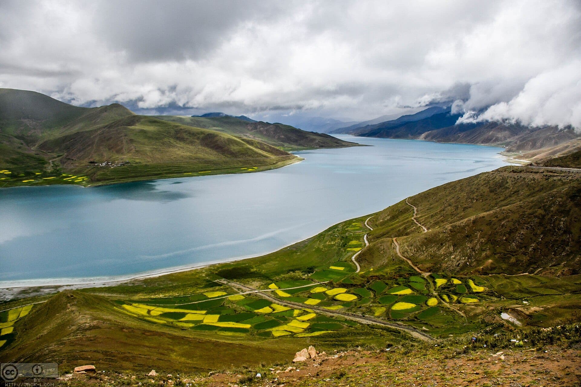 A turquoise high-altitude lake above terraced barley fields in Tibet